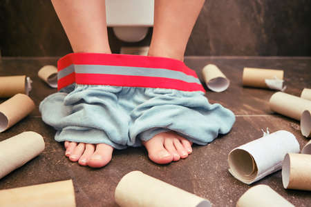 Problems with digestion, diarrhea, stomach pain in people. Woman feet with their underpants down and toilet paper strewn on the floorの写真素材