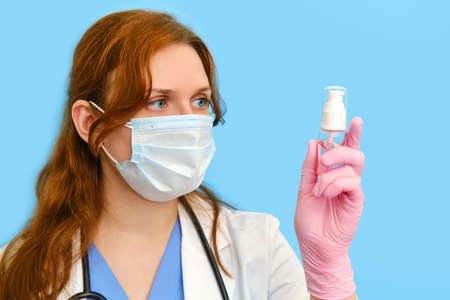 Woman doctor holding a sanitizer on a blue background, close-up.の写真素材