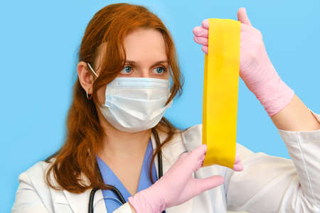 Woman nurse with elastic for sports stretching on a blue background, face closeup.の写真素材