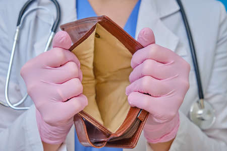 A doctor in medical gloves shows an empty wallet. Nurse in a white coat, the concept of the financial crisis due to coronavirusの写真素材