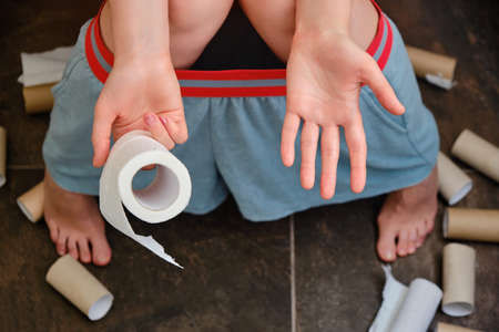 The woman has diarrhea and problems with stomach pain. Leftover toilet paper in hand, ended rolls are scattered on the floor.の写真素材