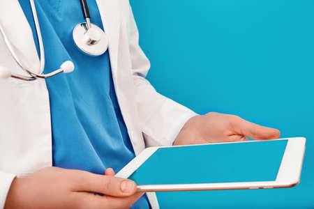 Doctor is looking into a digital tablet, close up. Female nurse in a white coat with a gadget in her hands. Concept of helping patients with coronovirus online.の写真素材