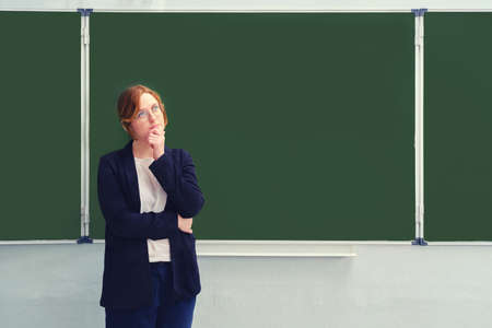 A school teacher stands doubtfully in front of an empty blackboard, copy space for the inscription. Problems with learning via the Internet during the flu virus epidemicの写真素材