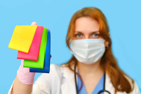 Woman doctor holds fitness elastic bands on a blue background, close-up.の写真素材