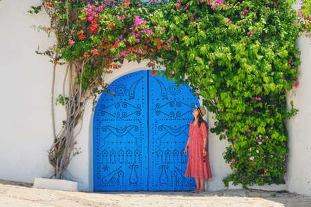 Woman next to home entwined liana with flowers in Sidi Bou Said, Tunisia - June 2019の写真素材