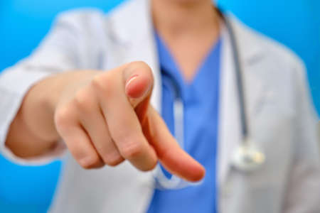 The doctor points his finger forward at you, close-up on a blue background. The nurse gestures with her hand - stay at home. Concept of treatment of the coronavirus epidemic in the worldの写真素材
