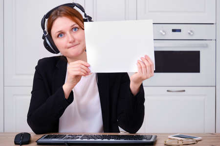 Businesswoman in a suit with a blank sheet in her hands during an online conference, copy space. A woman with headphones holds a blank form for the inscription, mockupの写真素材