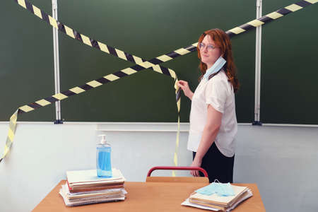 A teacher with a medical mask removed opens a school class. Concept for removing restrictions on schooling due to quarantine of coronavirusの写真素材