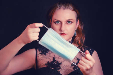 Vamp woman with medical mask, quarantine concept for halloween. Red-headed vampire woman holding a face maskの写真素材