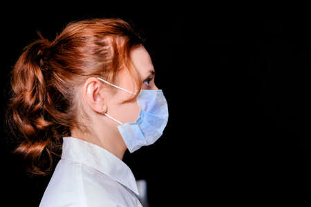 Young woman in a medical protective mask, face in profile. Closeup portrait of redhead woman during epidemic of coronavirus, copy space for text.の写真素材