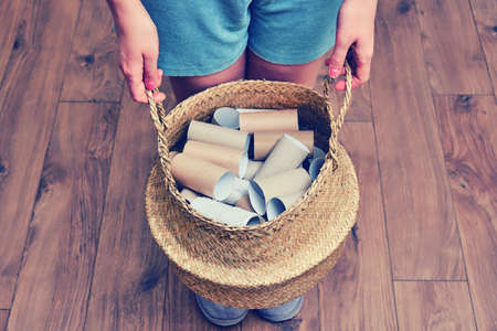 Female hands hold a basket with empty rolls of finished toilet paper. Cardboard recycling and reuse concept. Problems with toilet paper due to quarantine and isolation from coronavirusの写真素材