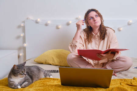 Problems with online education from home. Sad woman sitting with laptop on bed with catの写真素材