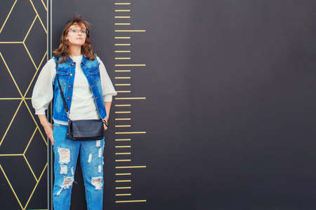 Girl stands next to a large scale ruler. Measurement of a woman in full growth. Man in denim near the wall with divisions. Copy space text conceptの写真素材