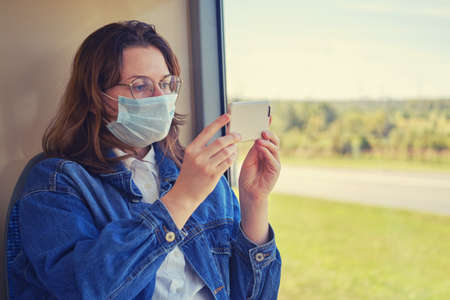 Woman traveling in a medical mask shoots a video on the phone from the transport. Tourism by public bus during an outbreak of coronavirusの写真素材