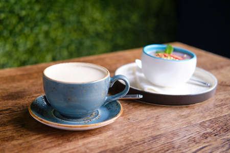 Blue cup of cappuccino coffee on a wooden table. Fruit dessert and drink in a summer cafe, close upの写真素材