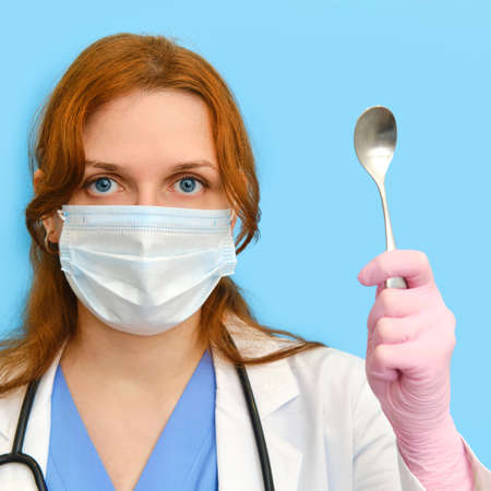 Woman nurse with a teaspoon on a blue background, closeup face.の写真素材