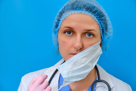 A doctor with wounds on his face takes off a medical mask. Nurse on a blue background with mask...
