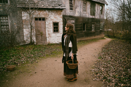 Young woman in vintage dress with wicker basket on the old street of a medieval cityの写真素材
