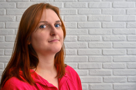 Portrait of a young redhead woman in red clothes on a background of a white brick wall