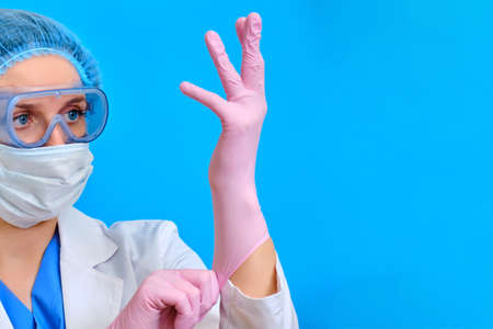 The doctor puts on protective gloves for working with patients with coronavirus, blue background. Nurse in a white coat and protective medical equipment, copy space. Influenza epidemic conceptの写真素材