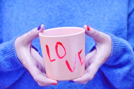 Woman in a blue sweater holds a pink cup with the inscription loveの写真素材