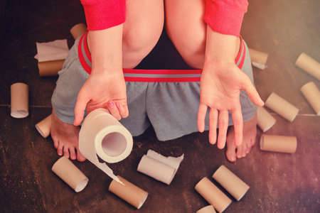 Concept of bowel disease, food poisoning and diarrhea problems. The rest toilet paper in hand, finished rolls are lying on the floorの写真素材