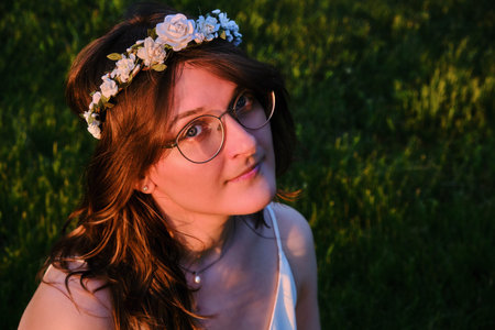 Young woman with a wreath of white flowers in the sunset. A girl in a white dress who looks like a fantasy characterの写真素材