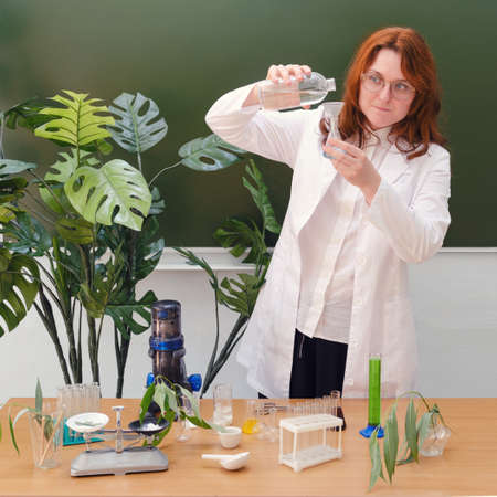 Cute woman teacher with bottle of water in school class at ecology lesson. Scientific research in the educational laboratory of the collegeの写真素材