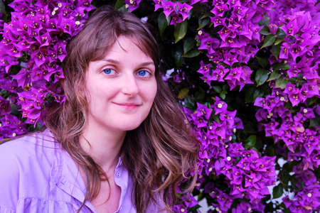 Young woman on a background of purple flowers, copy space. A girl smiles next to a tree blooming with violet flowers, face close-upの写真素材