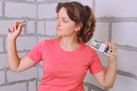 A young woman looks at the keys to the new apartment. Money and keys to the built house in hand. US dollars in exchange for new housing.の写真素材