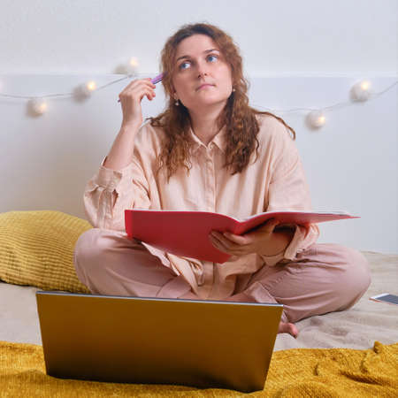 Sad girl sitting with laptop on bed. Problems with online education from homeの写真素材