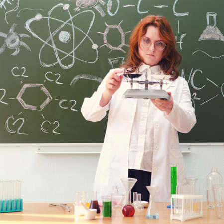 A woman physics teacher stands at the blackboard with weights in her hand. Physics lesson in a school class.の写真素材