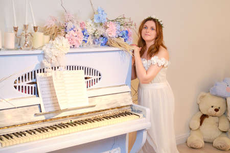 A female musician in a white dress stands next to a vintage blue pianoの写真素材