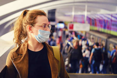 Woman in medical mask stands in the subway against the background of a crowd of people going to the stationの写真素材