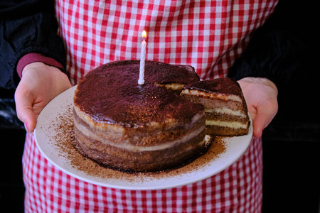 Woman holding a chocolate cake. Girl's hand with a plate on which lay the cakes. A lighted candle on...