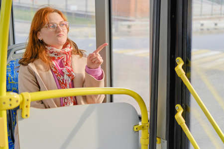 A red-haired woman rides a bus and points her finger at the roadの写真素材