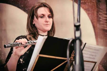 The flutist looks at the notes. Woman on stage with a flute. The musician looks at the notes on the music stand.の写真素材
