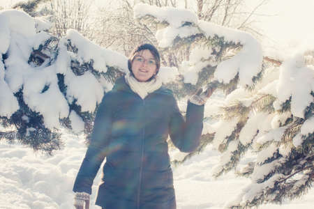 A woman smiles next to the snow covered branches of a fir tree in the forestの写真素材