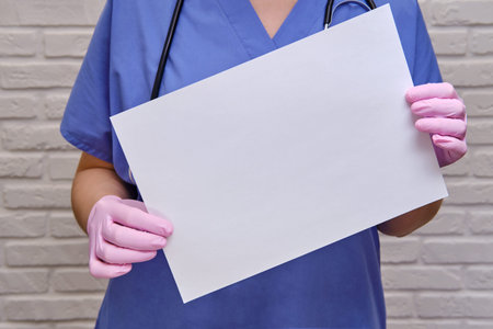 Doctor holds an empty blank sheet of paper, copy space for the inscription. Woman nurse in a blue...