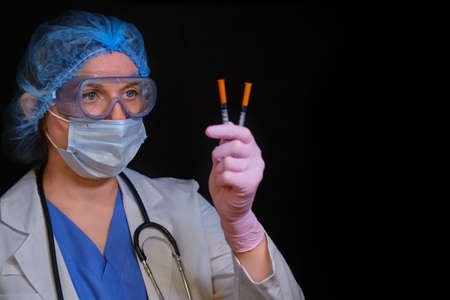 Female doctor with insulin syringes in hand on a black background, copy space for text. A nurse girl in a medical mask is preparing for an injection, conceptの写真素材