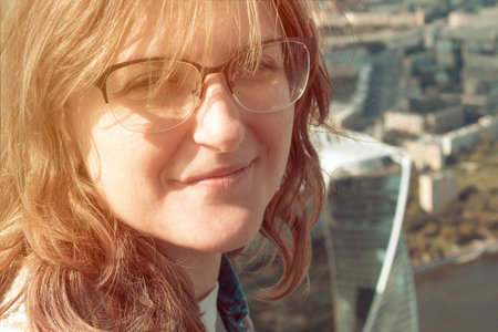 Female portrait on the background of the city. Girl face with glasses and curly hair in summer....