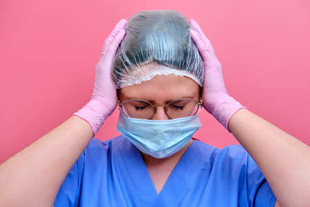 Young woman doctor in despair holding on to his head, concept. Portrait of a nurse on a pink background, close-up.の写真素材