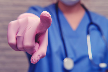 A doctor in protective gloves with a stethoscope points a finger forward on you, close-up