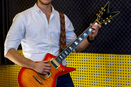 A guy in a white shirt with an electric guitar stands on the recording Studio. The guitarist plays...