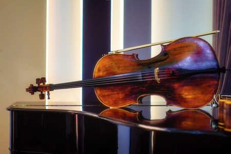 The violin lies on the piano and is reflected in the polished wood. Stringed musical instrument on the piano in the concert hall, before rehearsalの写真素材