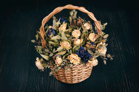 Retro basket with dry dead flowers on black background. The concept of old age and decay.の写真素材