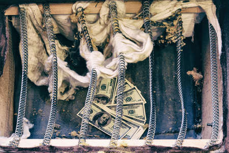 Money is hidden in an old spring sofa. Stash of us dollars in ancient furniture at homeの写真素材