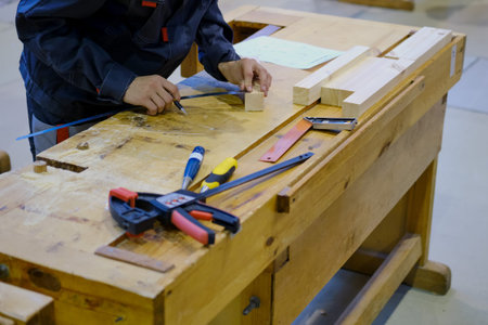 A carpenter measures a bar of wood with a ruler for carpentry on a workbench