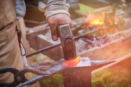 The blacksmith strikes the red blade of the sword with a hammer. Work in the forge to create weapons. The knife is between a rock and a hard place.の写真素材