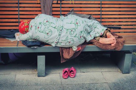 Grandma homeless in clean tidy clothes sleeping on a bench. Granny Stray in the city off his shoes and lay down on your belongings. In the city Park sleeping old lady homeless.の写真素材